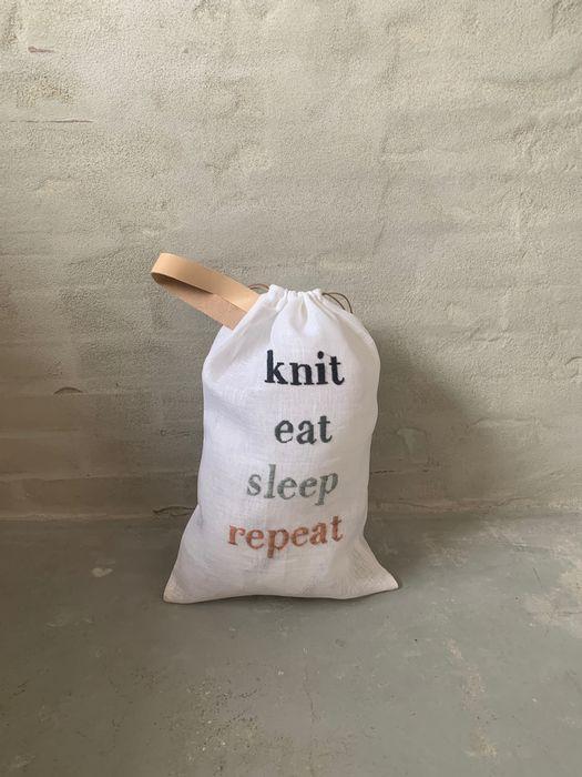 Strikkepose med broderi og teksten "Knit, eat, sleep, repeat", stående