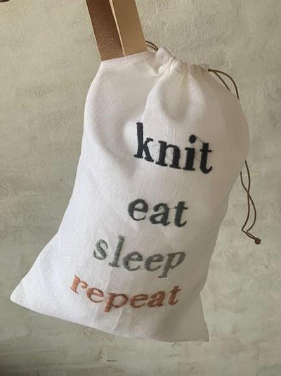 Strikkepose med broderi og teksten "Knit, eat, sleep, repeat", hængende